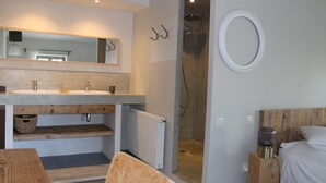A modern bathroom with a wooden vanity, dual sinks, a shower, and a bed with a wooden headboard. - La Grande Maison (Montmeyran)
