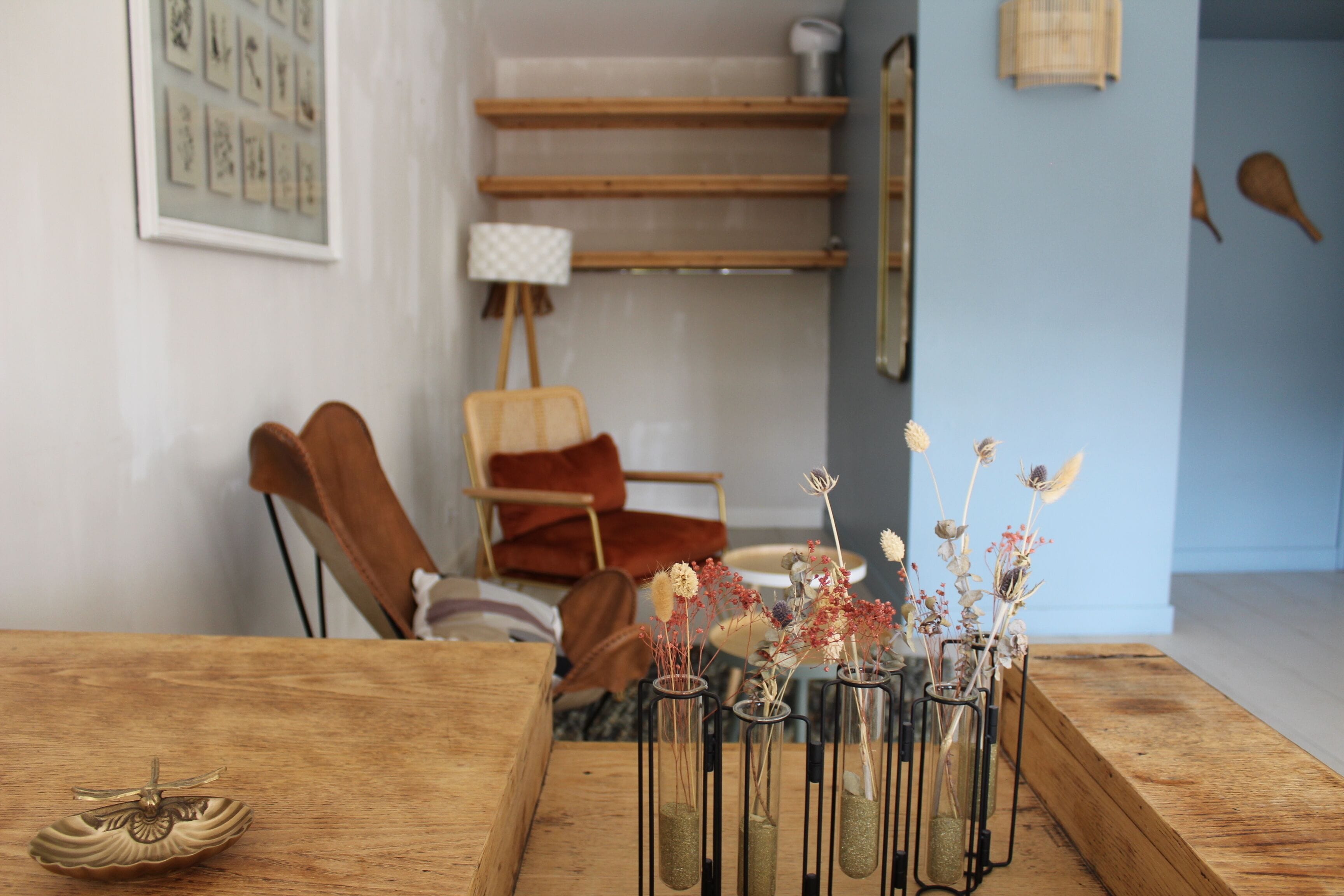 A wooden table with glass vases containing dried flowers, a brown chair, and a staircase in the background.