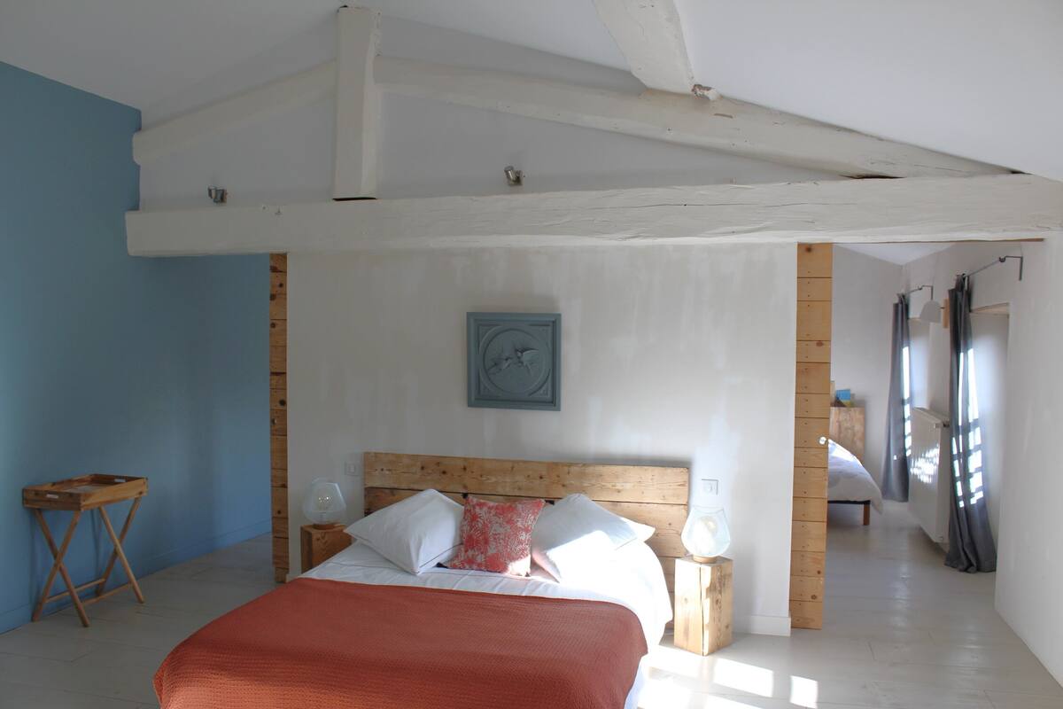 A bedroom with a wooden headboard, a bed with white and red bedding, a small wooden side table, and a nightstand with a lamp.