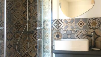 Une salle de bain avec des carreaux décorés, une douche en verre, un lavabo et un miroir.