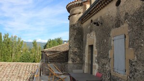 A rustic stone building with a tiled roof, a wooden table, and a red chair. - La Grande Maison (Montmeyran)