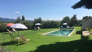 A backyard with a swimming pool, green lawn, and lounge chairs under umbrellas. - La Grande Maison (Montmeyran)