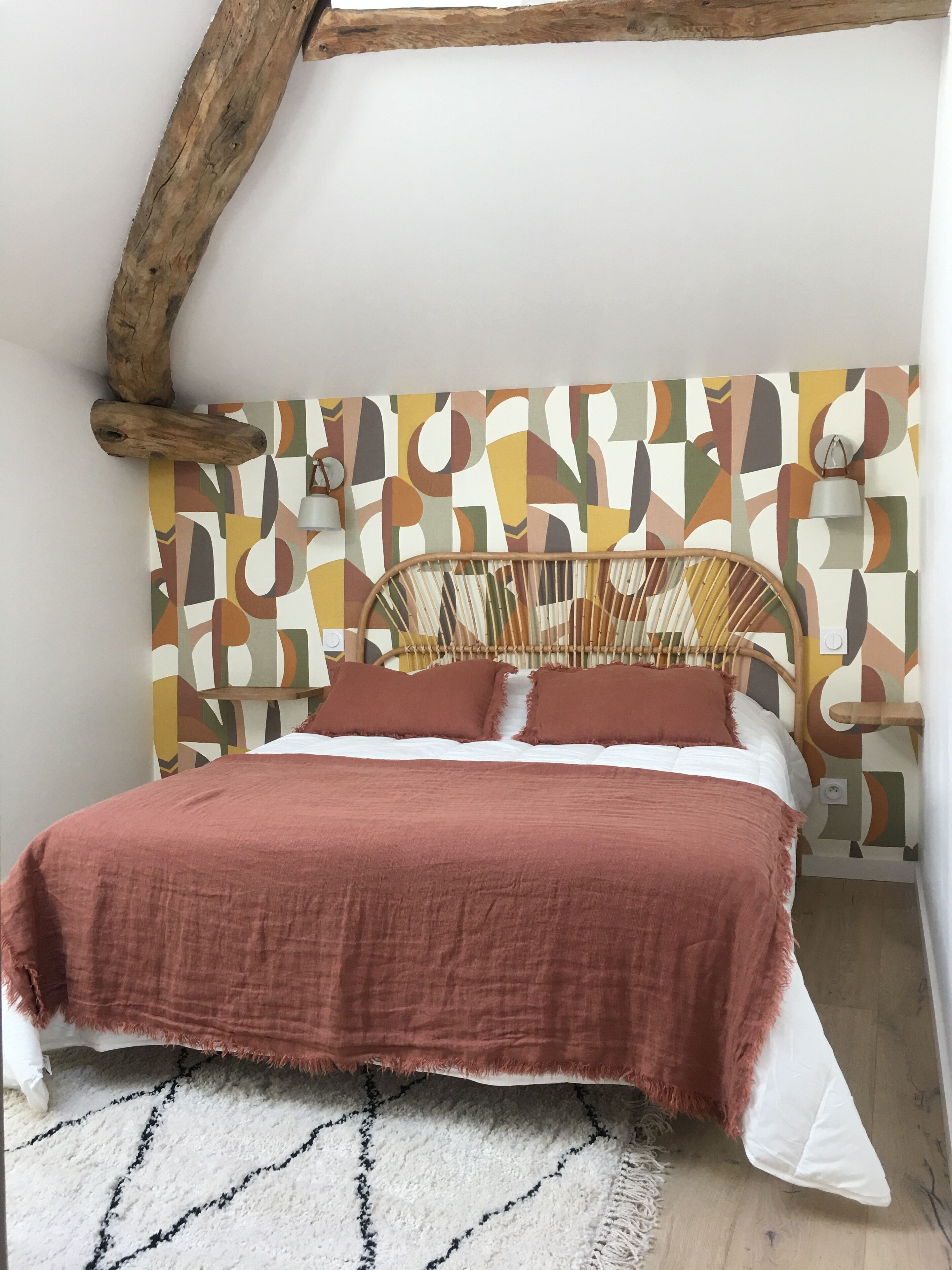A bed with a wooden headboard, a patterned wall, and a white rug.