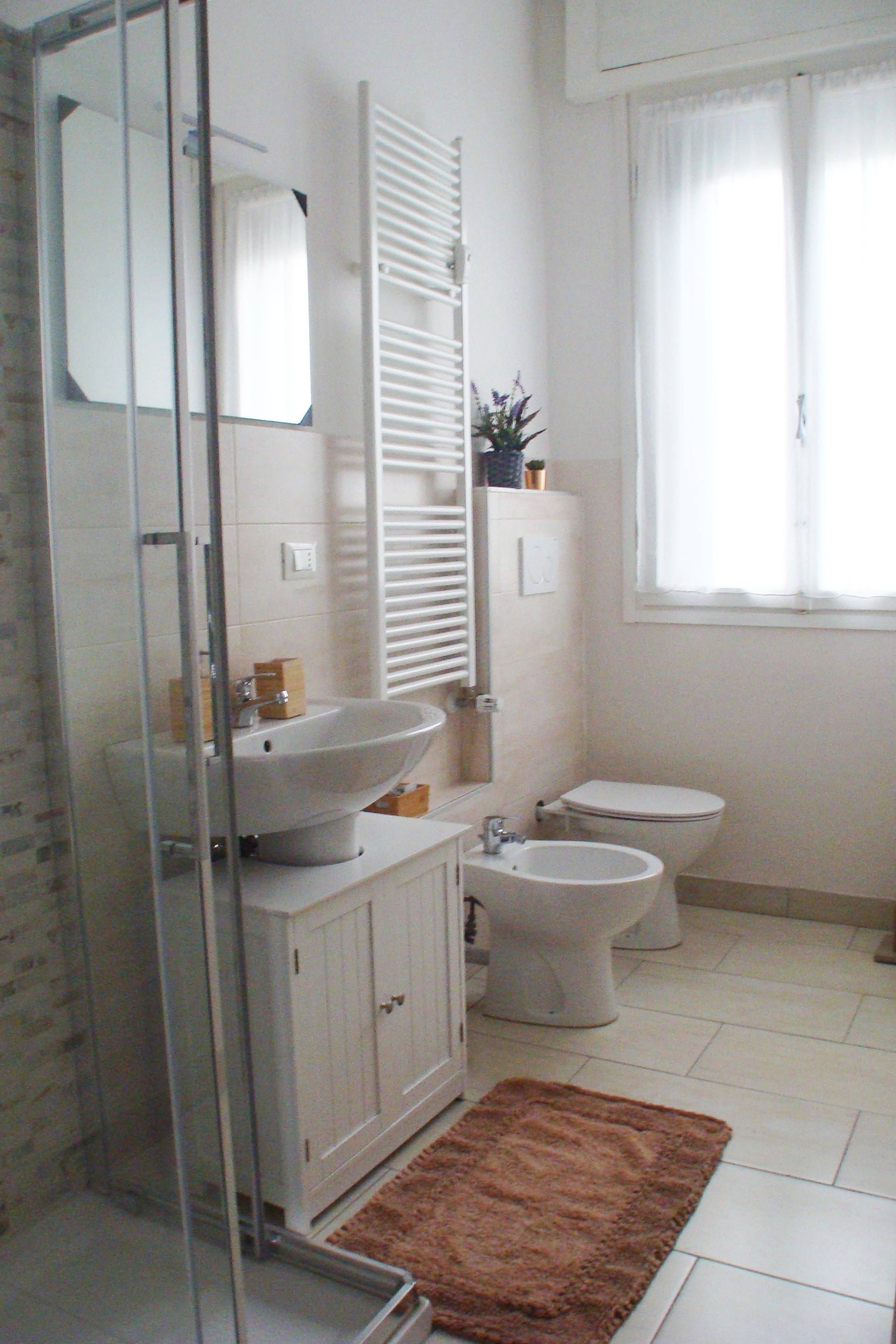 A bathroom with a glass shower enclosure, a sink, a toilet, and a bidet.