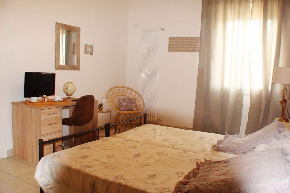 Une chambre à coucher avec un lit, un bureau avec un ordinateur, une chaise, un globe terrestre et une fenêtre avec des rideaux.