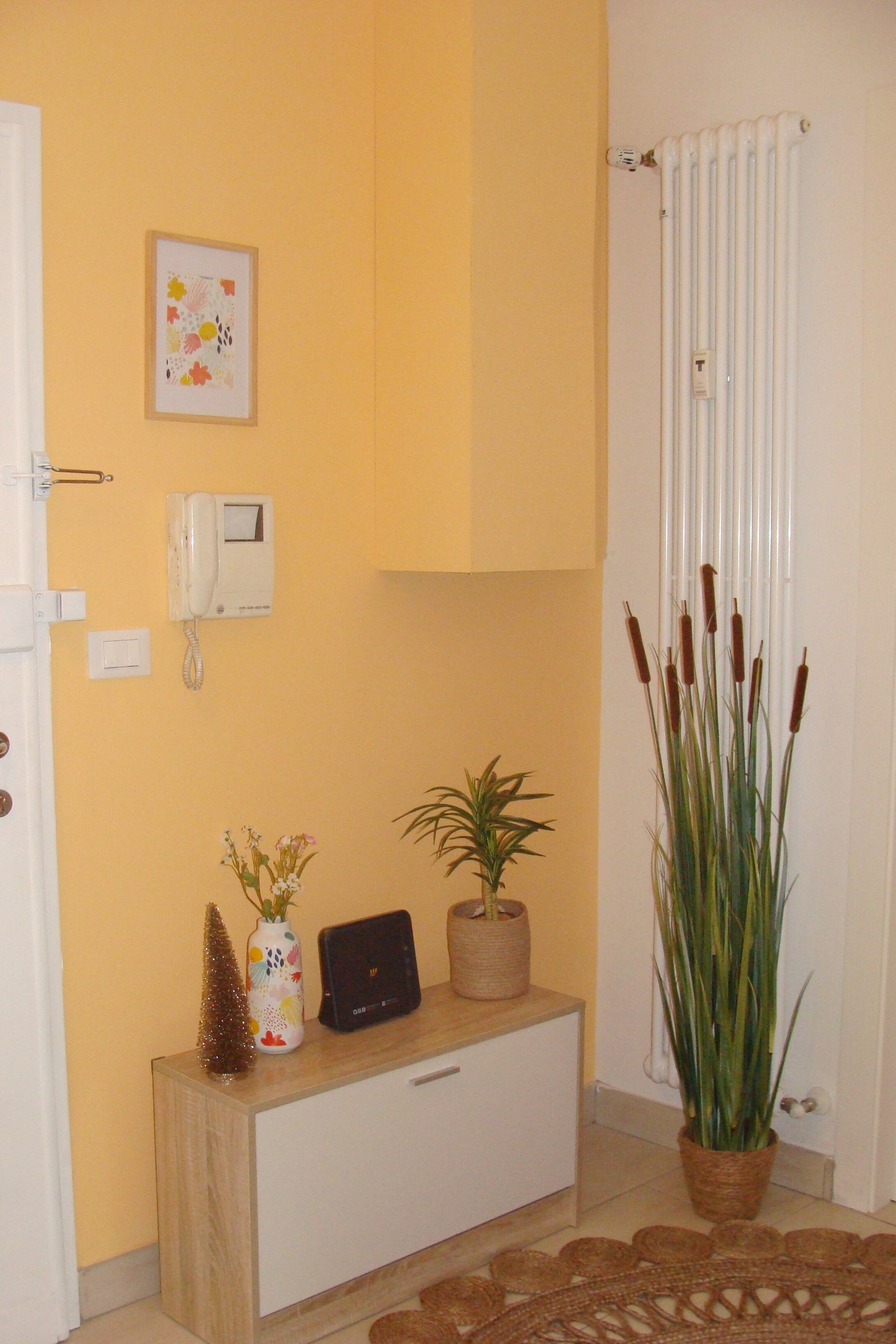 A hallway with a wooden console table, a potted plant, a framed picture, a thermostat, and a radiator.