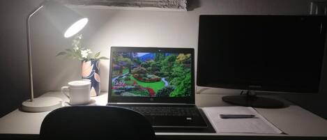 Un escritorio con una computadora portátil, un monitor de escritorio, una lámpara, una taza y una planta.