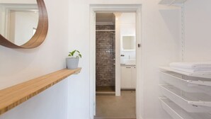 A hallway with a wooden shelf, a potted plant, a mirror, and a bathroom with a brick wall, sink, and towel racks. - Koala at White Gum Lodge (White Gum Valley)