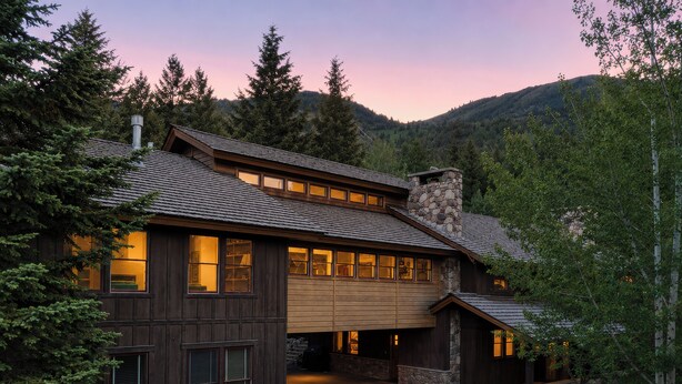 A two-story log cabin with a stone chimney, large windows, and a driveway leading to the entrance. - Trinity :Sleeps 10- HotTub-GameRoom-Huge Kitchen-Perfect4Groups Tram & Mtn View (Teton Village)