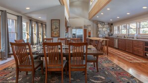 A spacious dining area with a high ceiling, large windows, and a stone accent wall. - Trinity :Sleeps 10- HotTub-GameRoom-Huge Kitchen-Perfect4Groups Tram & Mtn View (Teton Village)