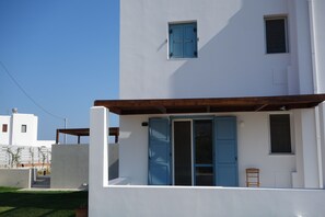 Um edifício moderno branco com persianas azuis, uma pérgula de madeira e uma pequena cadeira de madeira.