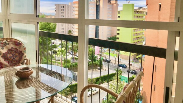 A balcony with a glass table and a chair, overlooking a street with cars and buildings. - GREAT APARTMENT FOR HOLIDAY RENT RINCON DE LOIX R059 (Benidorm)