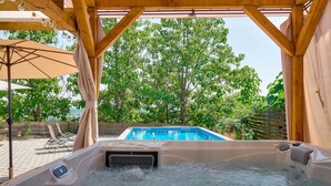 Un bain à remous avec vue sur une piscine et des arbres.