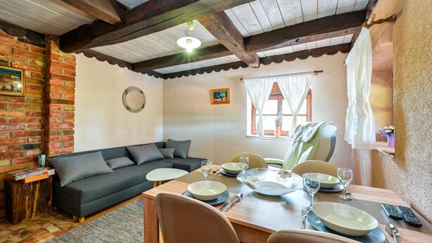 Un salon chaleureux avec un canapé gris foncé, une table à manger en bois dressée pour deux personnes et un mur en briques au style rustique.