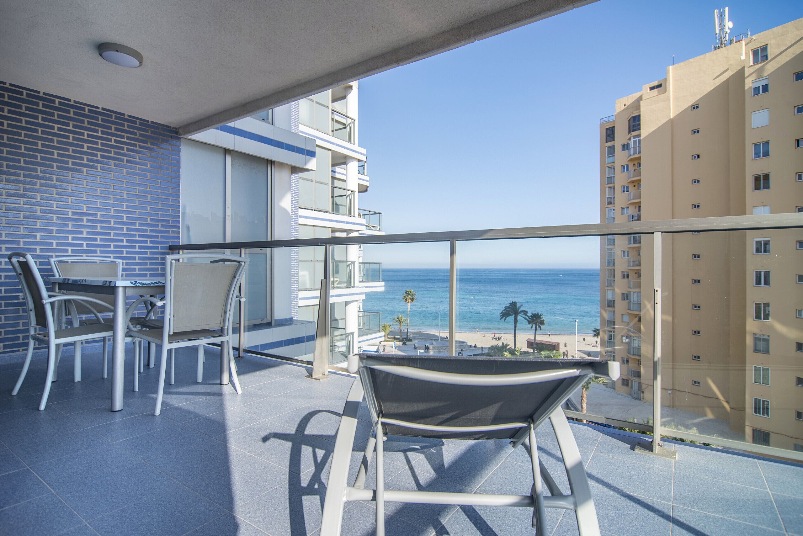 Un balcone con vista sull'oceano, un'area pranzo con sedie e un edificio con un muro in piastrelle blu.