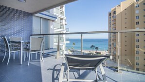 Un balcone con vista sull'oceano, un'area pranzo con sedie e un edificio con un muro in piastrelle blu.