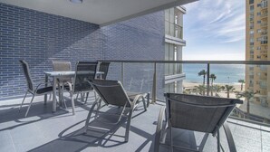 Ein Balkon mit Tisch und Stühlen, Blick auf den Strand und ein hohes Gebäude im Hintergrund.