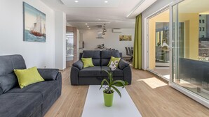 Una sala de estar moderna con un sofá gris, una planta verde y un comedor al fondo.