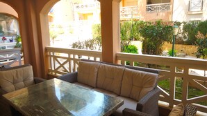 A balcony with wicker furniture and a glass table, overlooking a courtyard with plants and a building in the background. - Edison Bungalow LEK (Peñiscola)