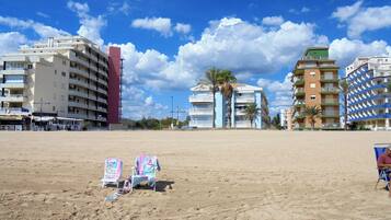 A beach with a row of multi-story buildings, some with balconies, and a few palm trees.