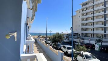 A coastal street with parked cars, a building with balconies, and a clear view of the sea.