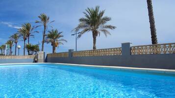 A swimming pool with clear blue water, surrounded by palm trees and a decorative fence.