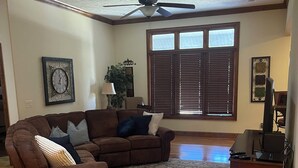 A living room with a sectional sofa, a ceiling fan, a large window with blinds, and a decorative rug. - Golf Getaway-Large Families Welcome! Only 10 minutes from the Airport!  (Springfield)