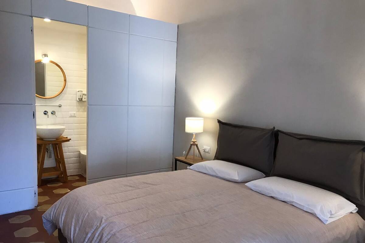 A bedroom with a bed, a bedside lamp, and a bathroom visible through an open door.