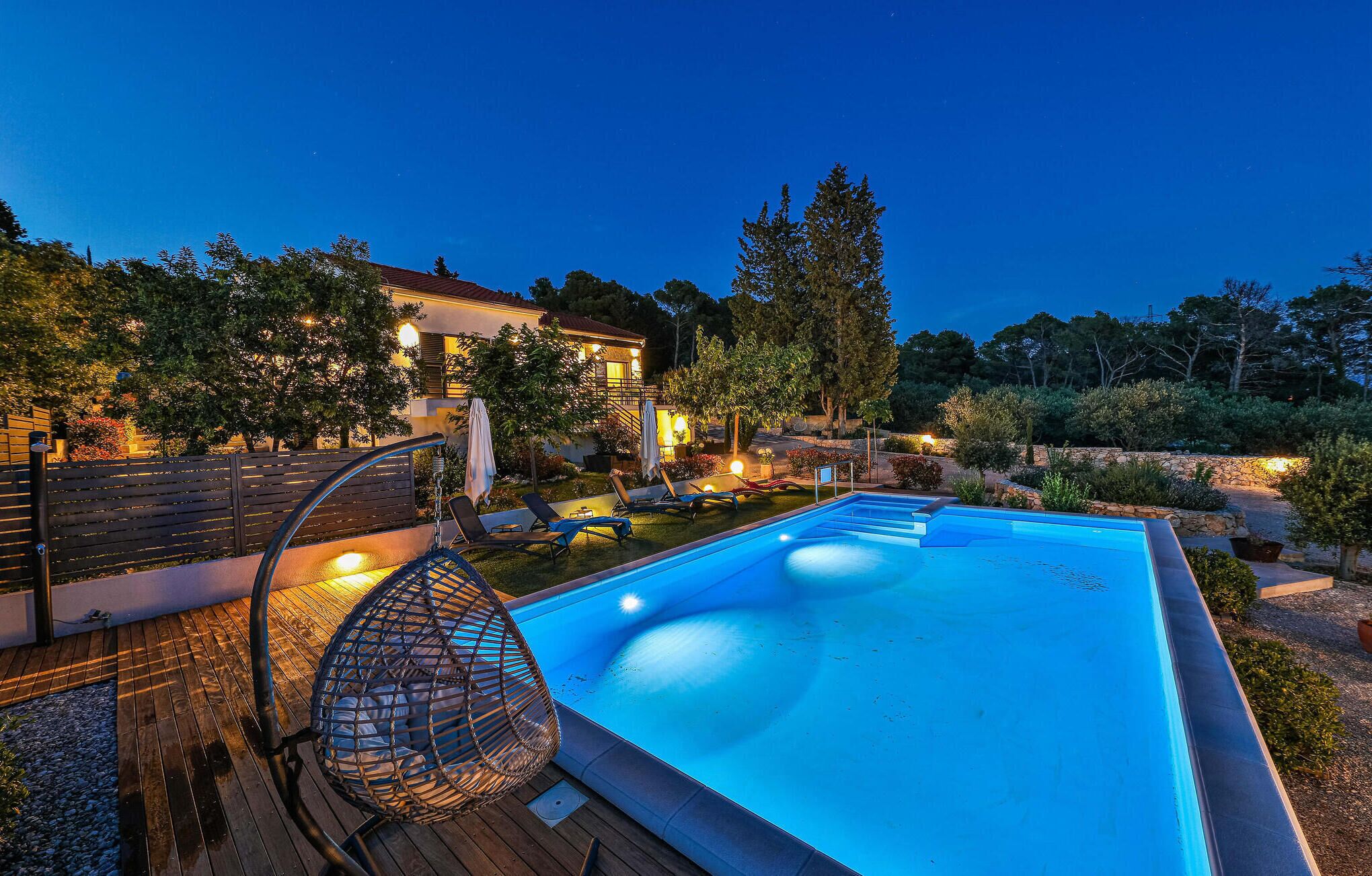 Ein Pool mit Holzterrasse, Liegestühlen und einem Haus im Hintergrund.