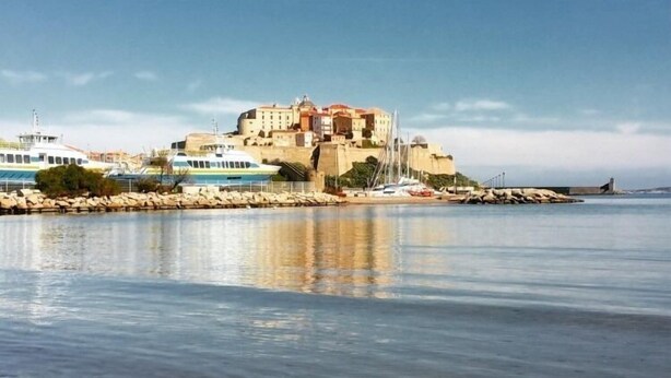A coastal building with a waterfront view, a clear sky, and calm water. - Studio Orsoni - See View (Calvi)