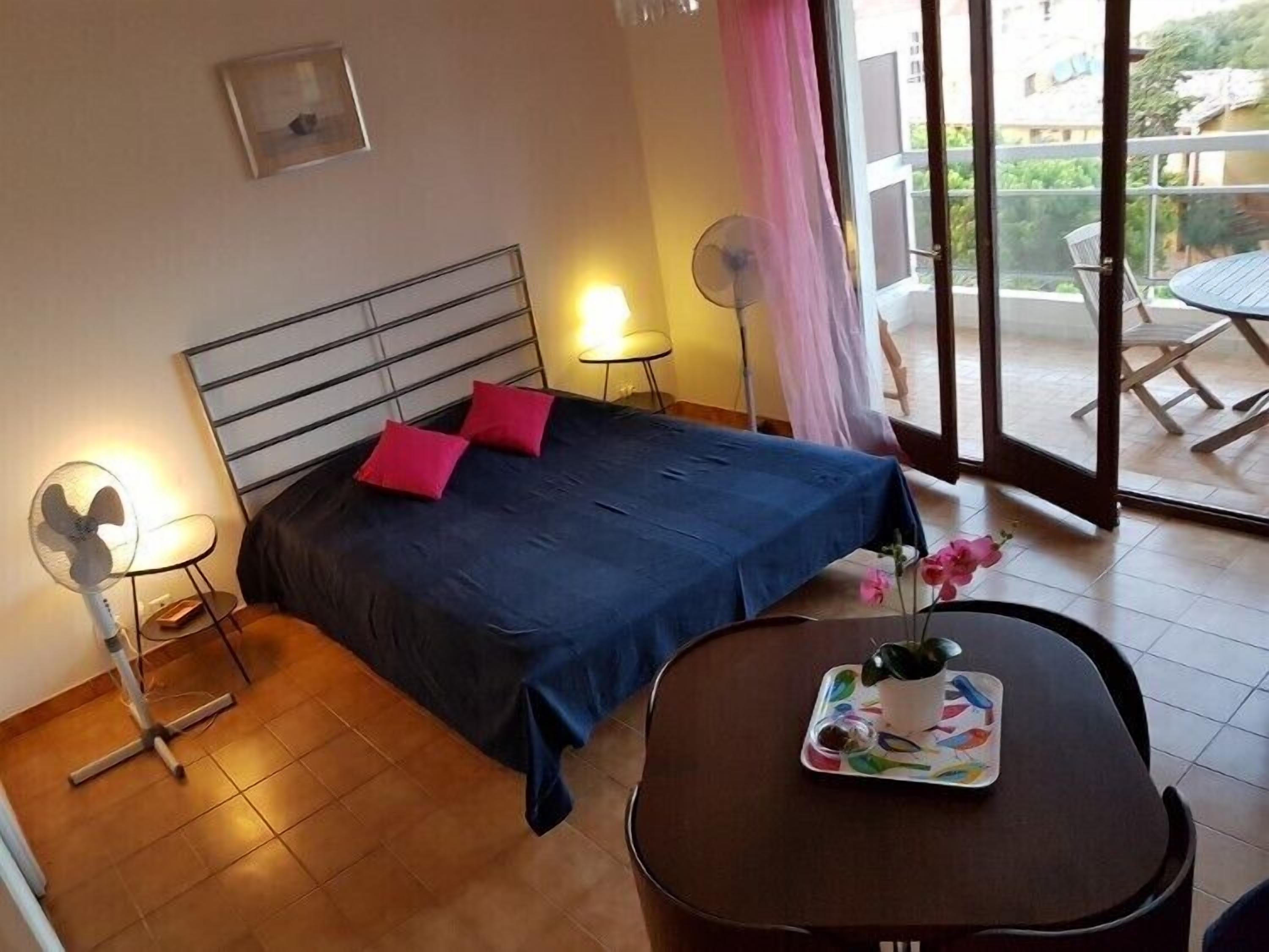 Een slaapkamer met een bed, nachtkastjes, een ventilator en een tafel met een dienblad.