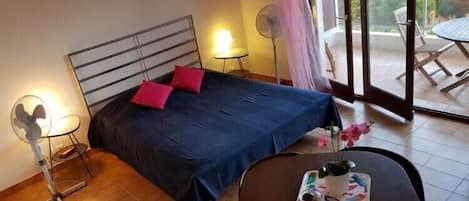 A bedroom with a bed, bedside tables, a fan, and a table with a tray.