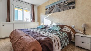 Een slaapkamer met een groot bed, een raam met gordijnen, een nachtkastje met een lamp en een schilderij aan de muur.