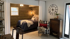 Un dormitorio con cama, silla, reloj y ventana.