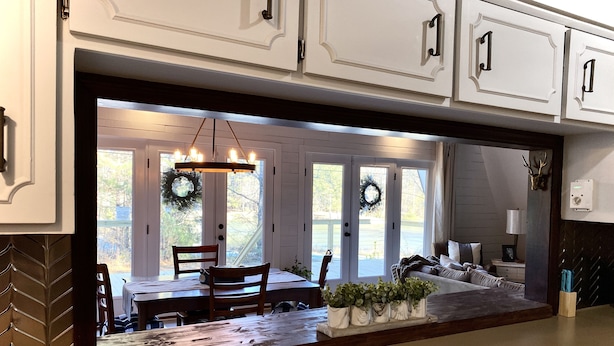 Una cocina con armarios blancos, encimera de madera y vista hacia un comedor con mesa y sillas.