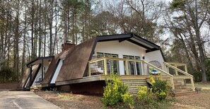 Ein Haus mit geneigtem Dach, einer Veranda mit Geländer und einem Fenster mit Blick auf den umliegenden Wald.