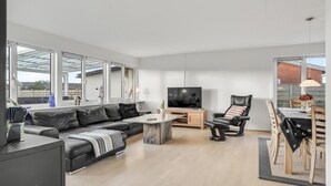 A modern living room with a sofa, a TV, a dining table, and a chair. - 2 bedroom lovely home in Thisted (Thisted)