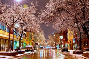 A snow-covered street at night with illuminated buildings and trees.