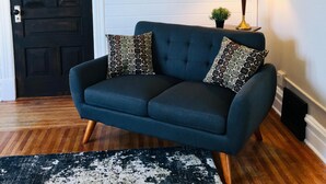 A dark blue sofa with patterned pillows, a round mirror, a small plant, and a black and white rug in a room with wooden flooring and a dark door. - Close to everything! DISCOUNTS for Long Stays- Fully Remodeled (Eau Claire)