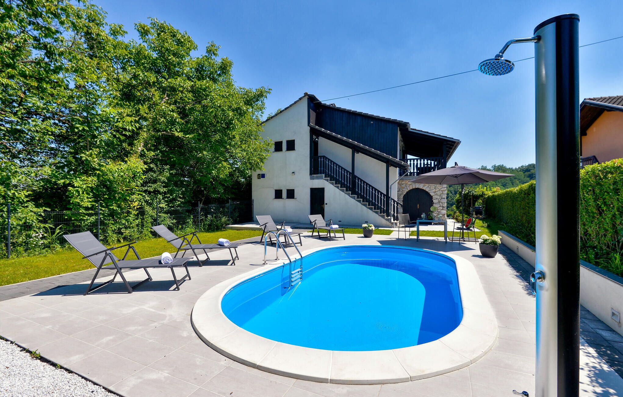Piscina moderna ao ar livre com espreguiçadeiras, área de estar coberta e escadaria de pedra que leva a um segundo andar.