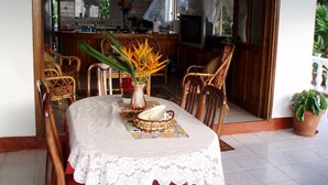A dining area with a table set for two, surrounded by wooden chairs. A vase with flowers is on the table.
