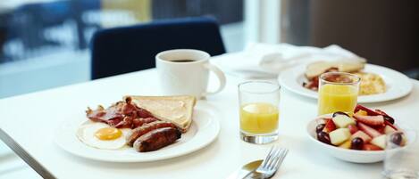 A breakfast table with toast, eggs, sausages, bacon, coffee, orange juice, and a fruit bowl.