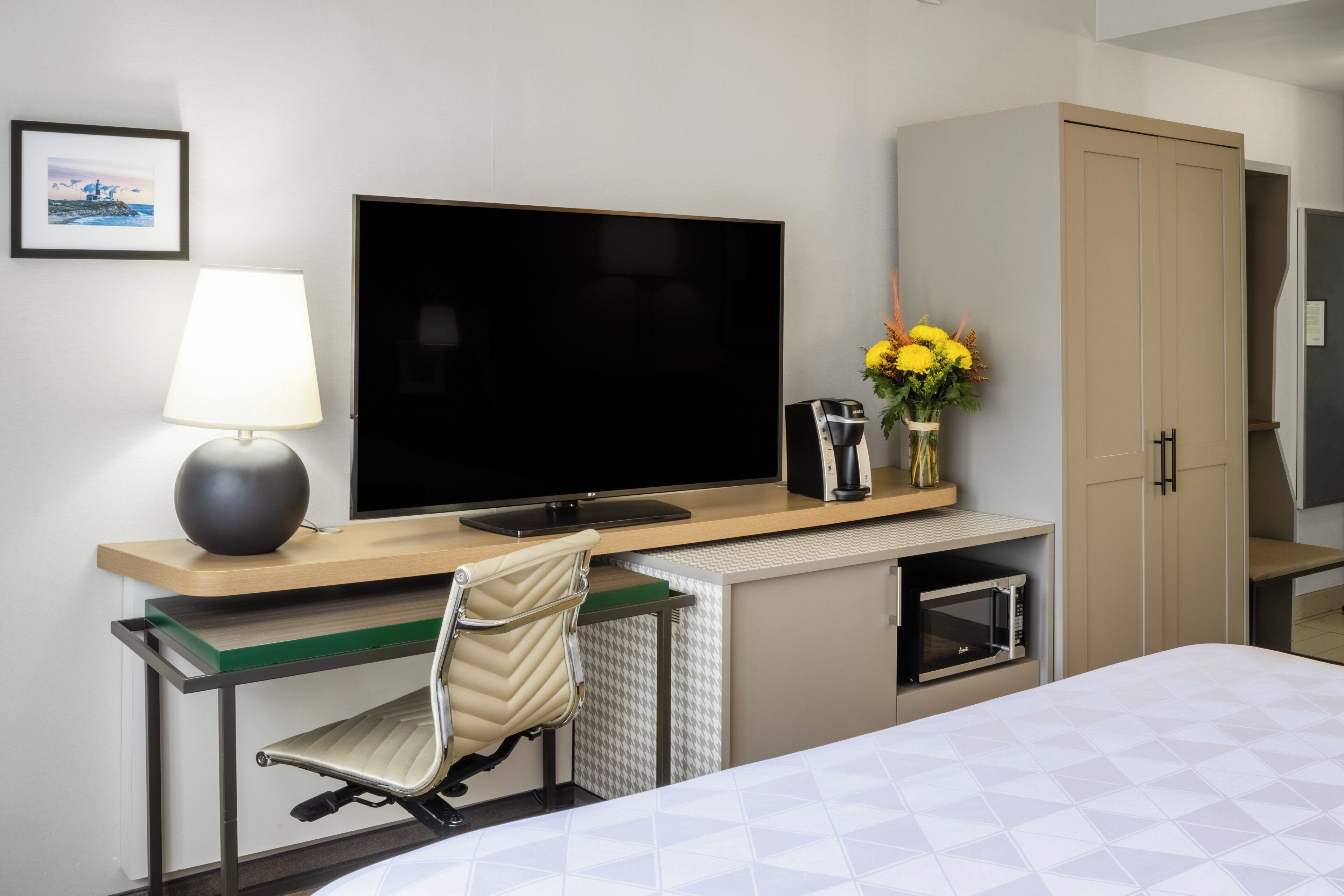 Habitación de hotel con cama, escritorio con computadora, televisor, lámpara, microondas y mueble.