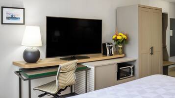 Habitación de hotel con cama, escritorio con computadora, televisor, lámpara, microondas y mueble.