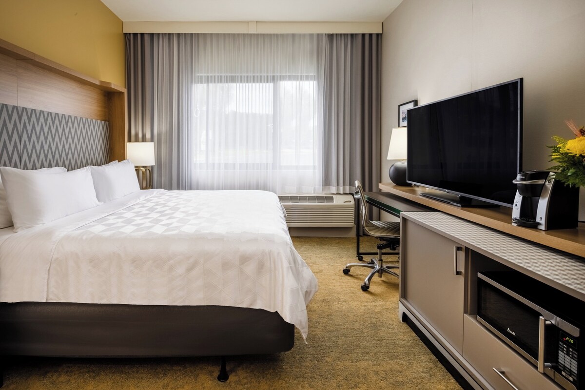 Une chambre d’hôtel dotée d’un grand lit, d’un téléviseur à écran plat, d’un bureau avec un ordinateur et d’une machine à café.
