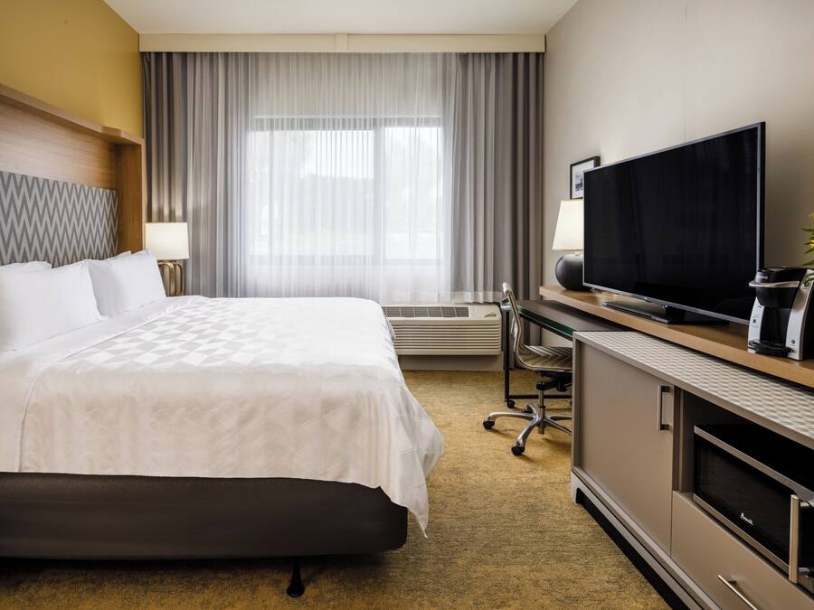 A hotel room with a large bed, a flat-screen TV, a desk with a computer, and a coffee maker.