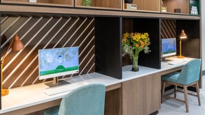 Un espacio de oficina moderno con dos escritorios, cada uno con un monitor de computadora, teclado y un jarrón de flores.