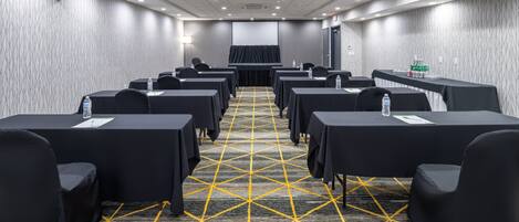 Une salle de conférence avec des rangées de tables, des chaises et une scène.