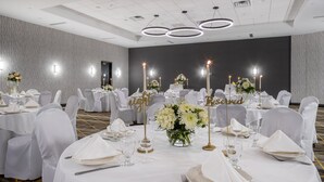 Un salón de banquetes con mesas redondas dispuestas para un evento formal, con manteles blancos, detalles dorados y centros de mesa florales.