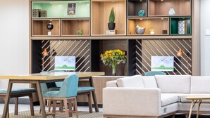 Un área de recepción moderna con un escritorio de madera, dos monitores de ordenador, un sofá y una estantería decorativa con varios objetos.